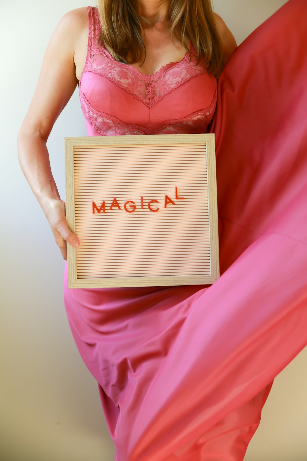 Woman in pink dress holds a sign saying magical.