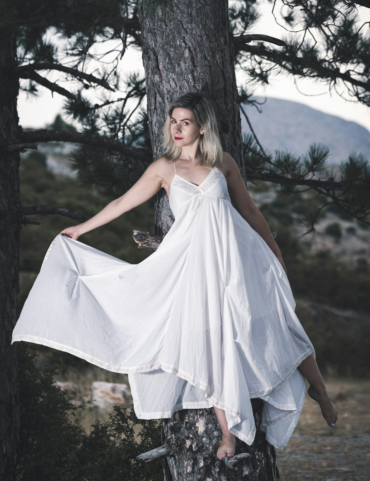 woman in white sleeveless dress standing on brown tree