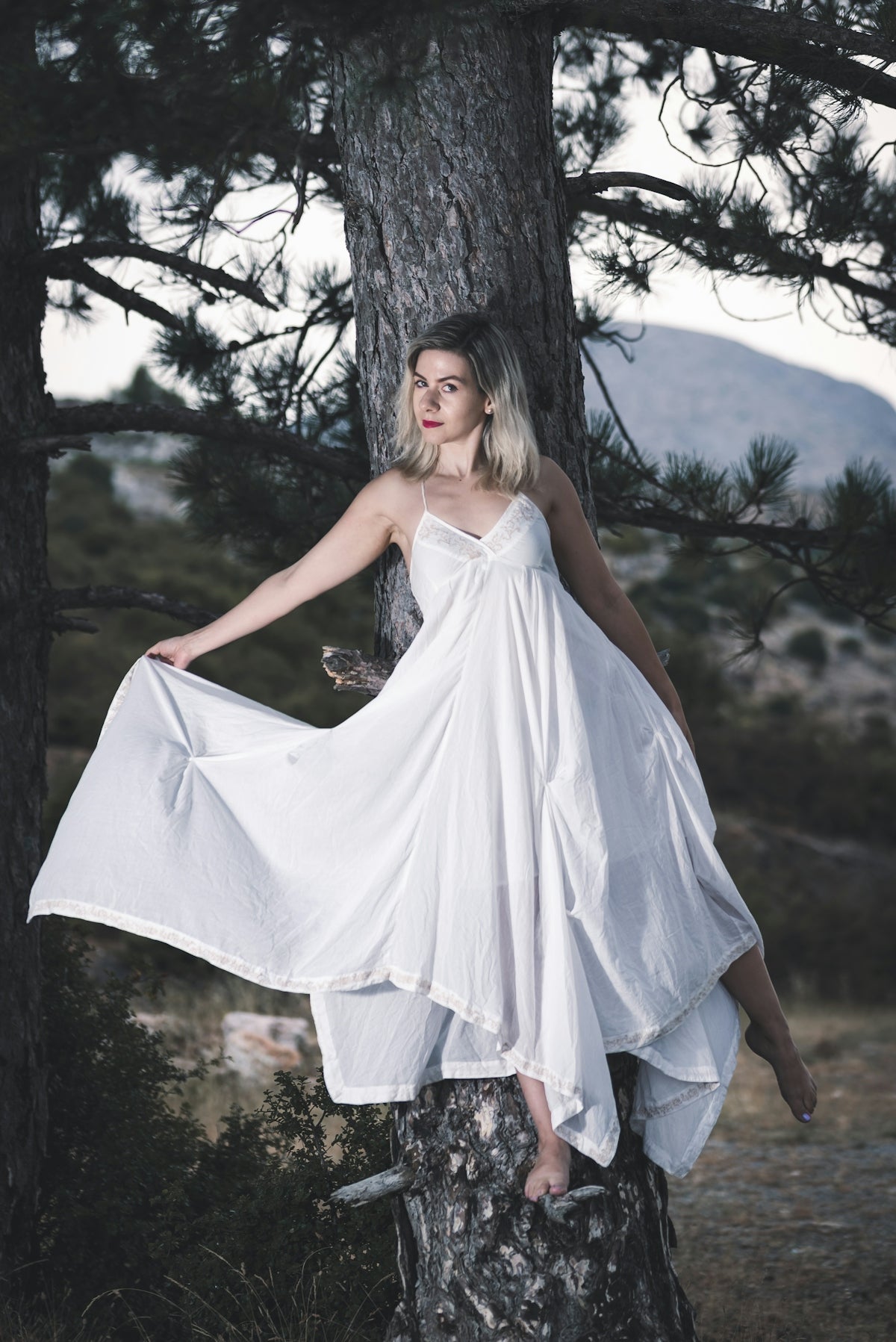 woman in white sleeveless dress standing on brown tree