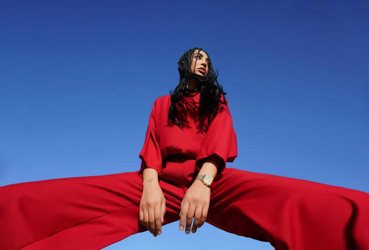 A woman with braided hair in a red outfit against a clear blue sky