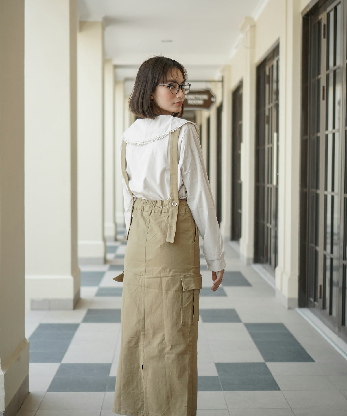 A woman standing in a hallway wearing a white shirt and khaki skirt