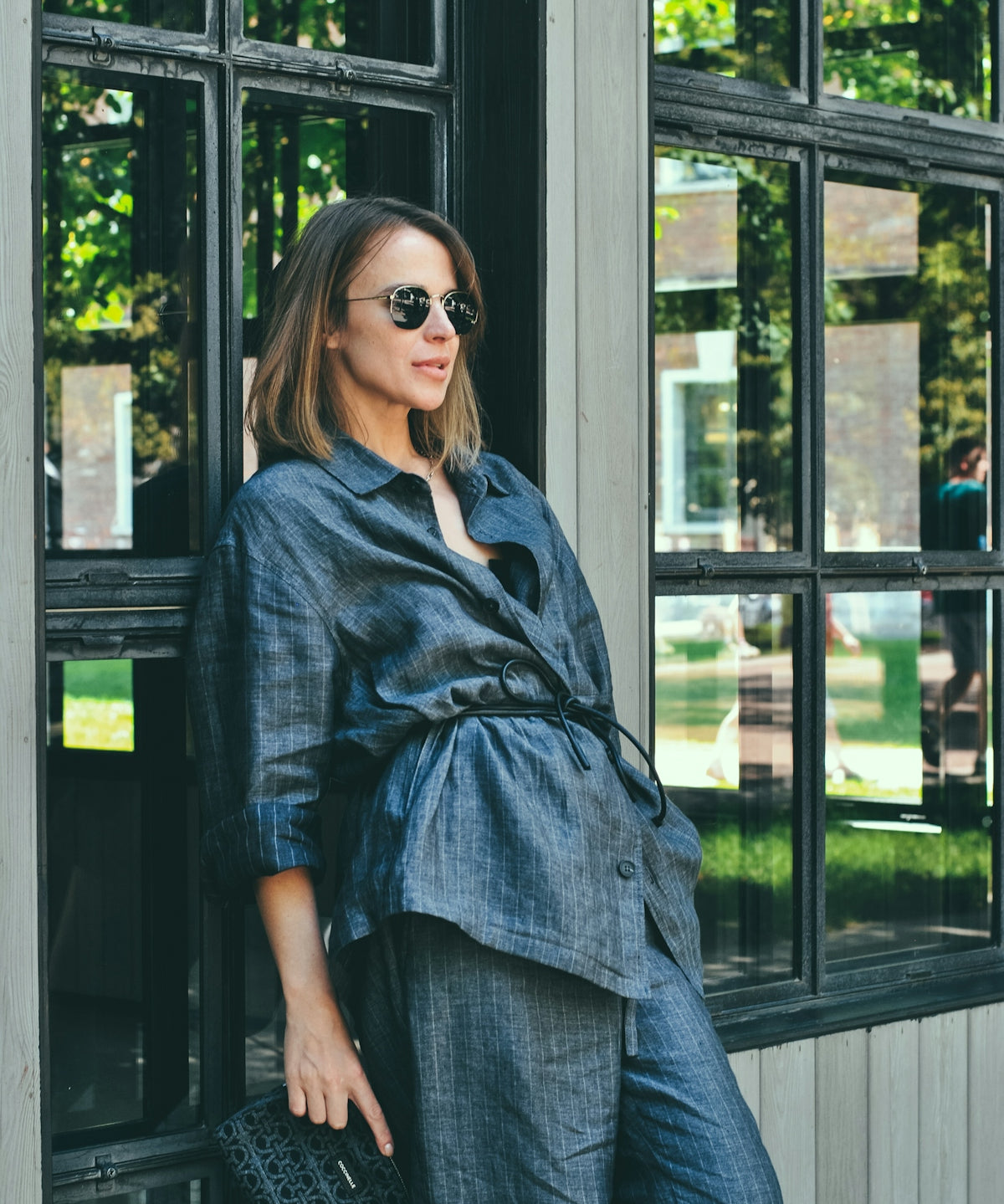 Woman in denim outfit poses by a window.