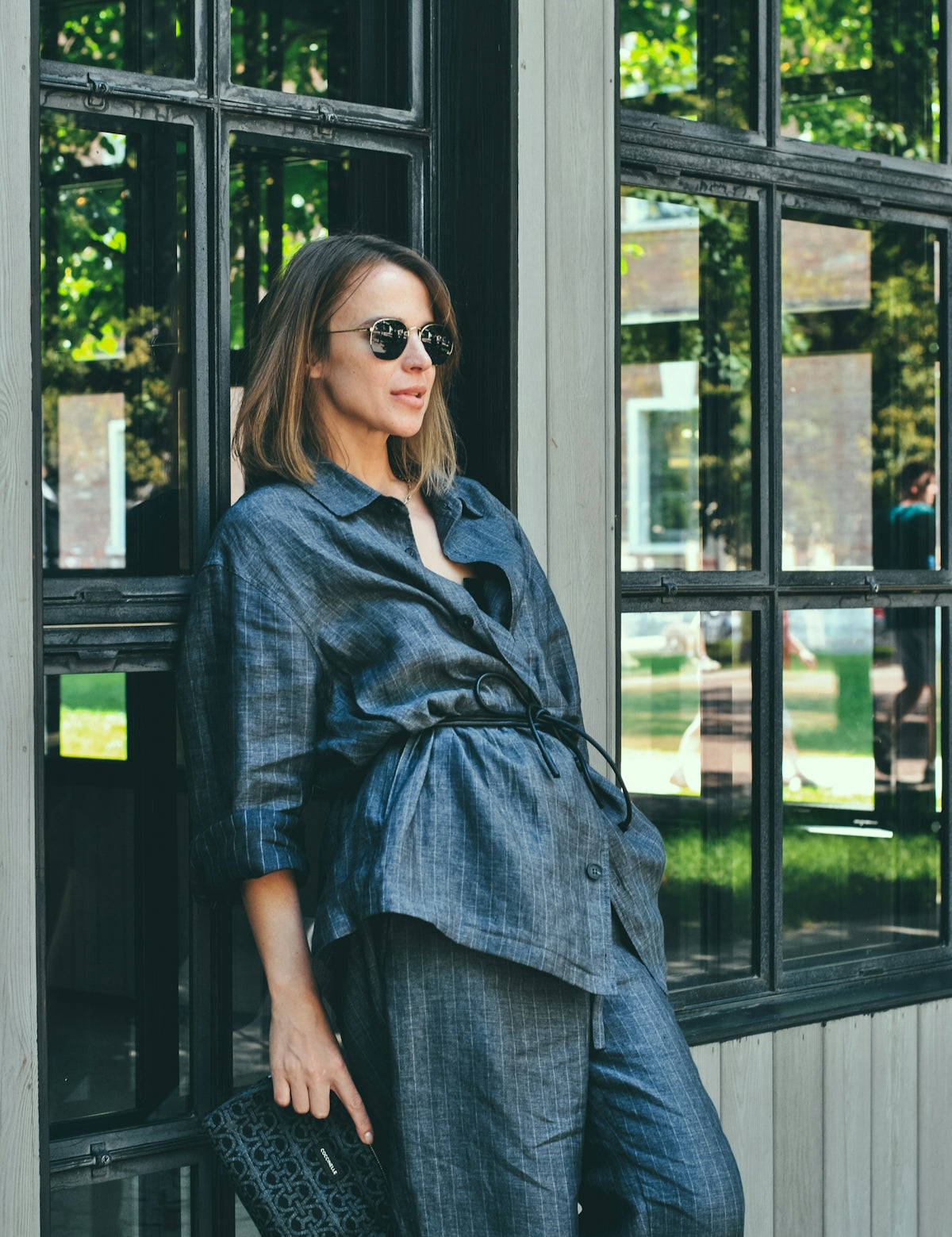 Woman in denim outfit poses by a window.