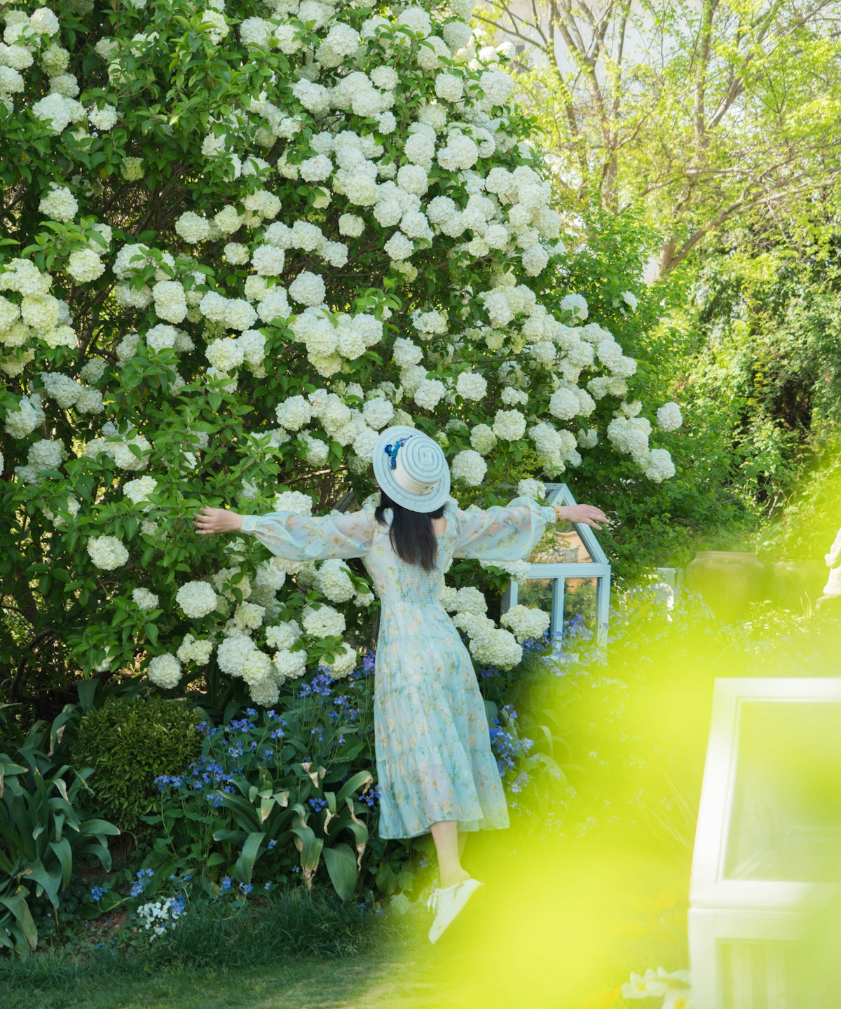 Woman stands near a blooming bush with open arms.