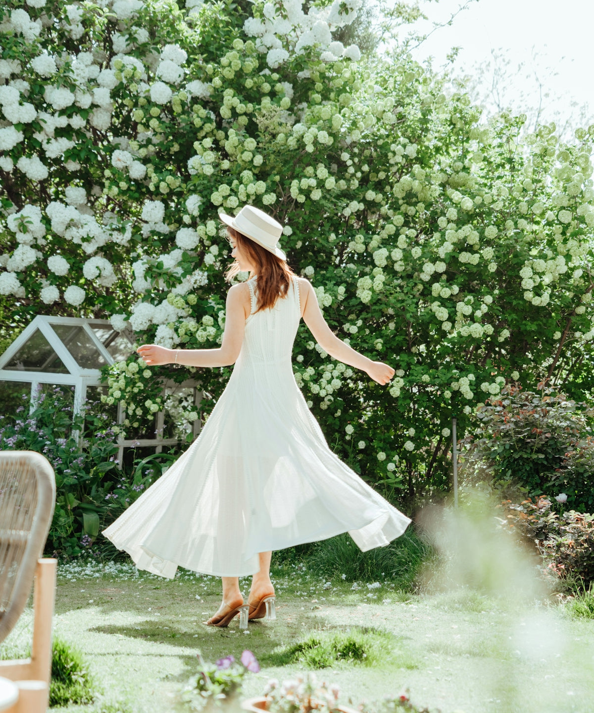 Woman twirling in a white dress in a garden.