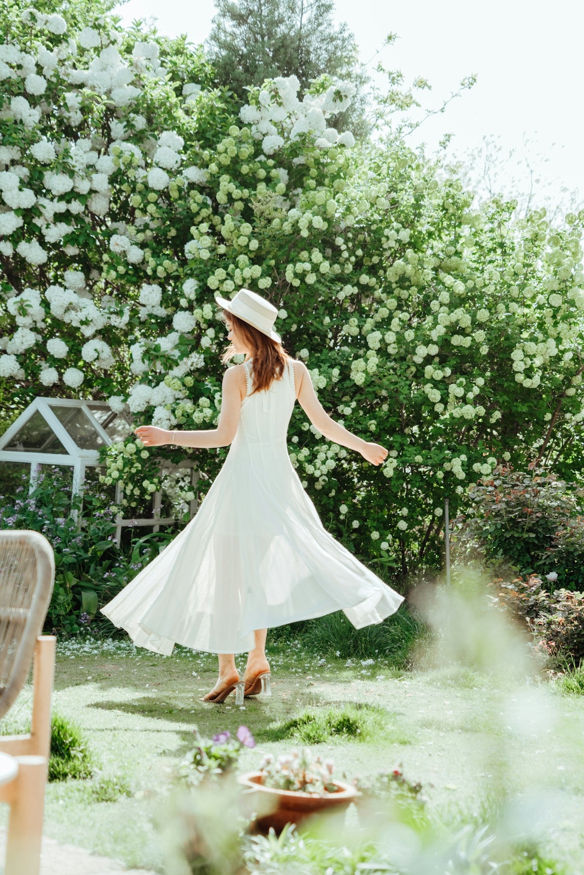 Woman twirling in a white dress in a garden.