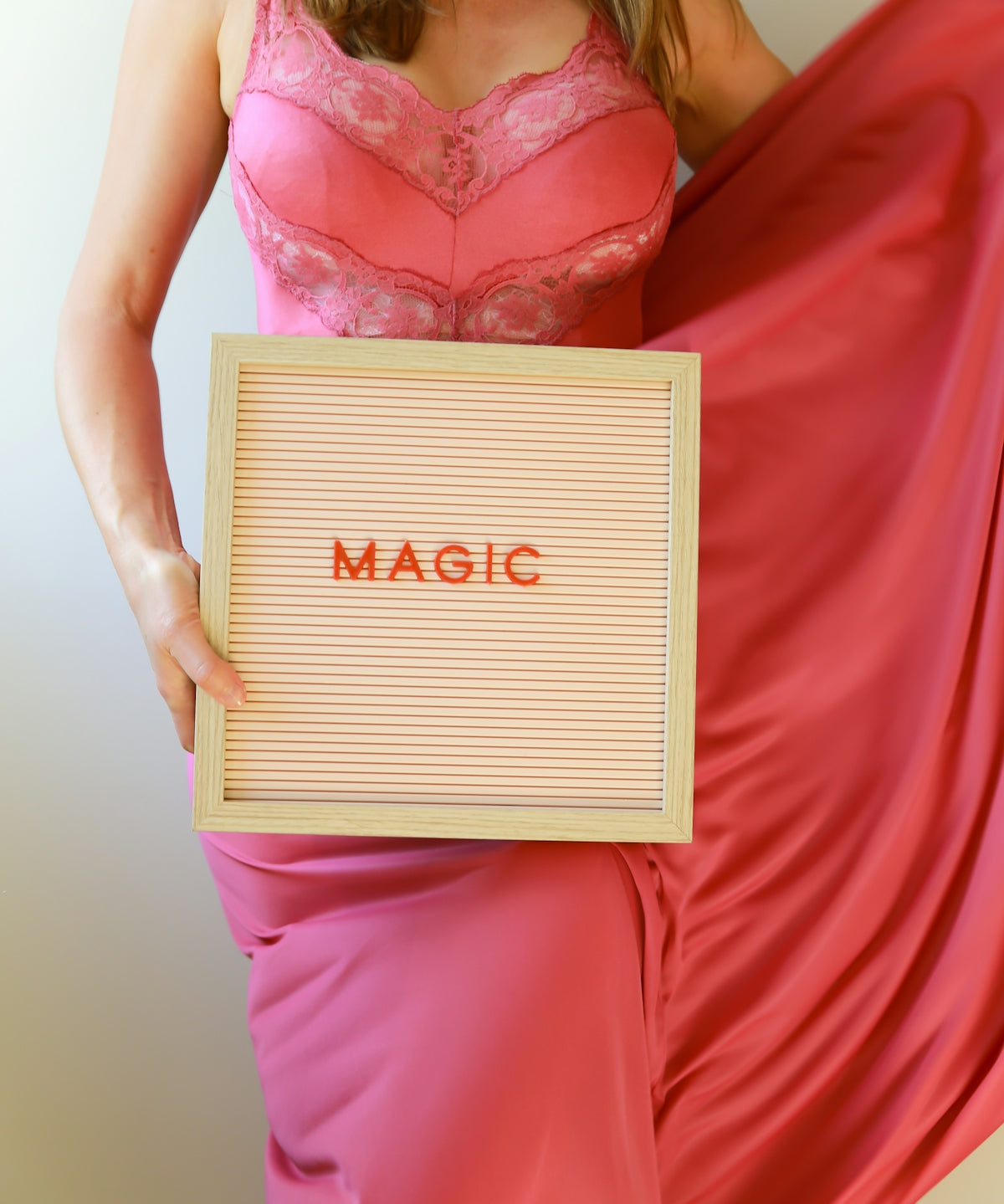 Woman in pink dress holds a sign reading magic.