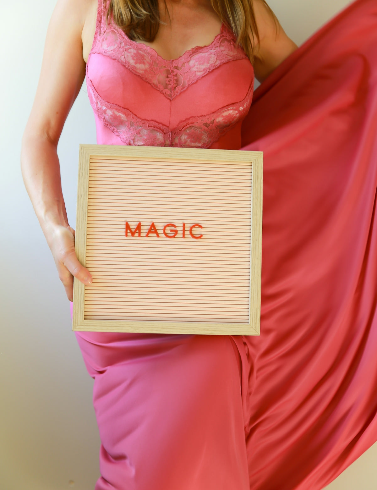 Woman in pink dress holds a sign reading magic.