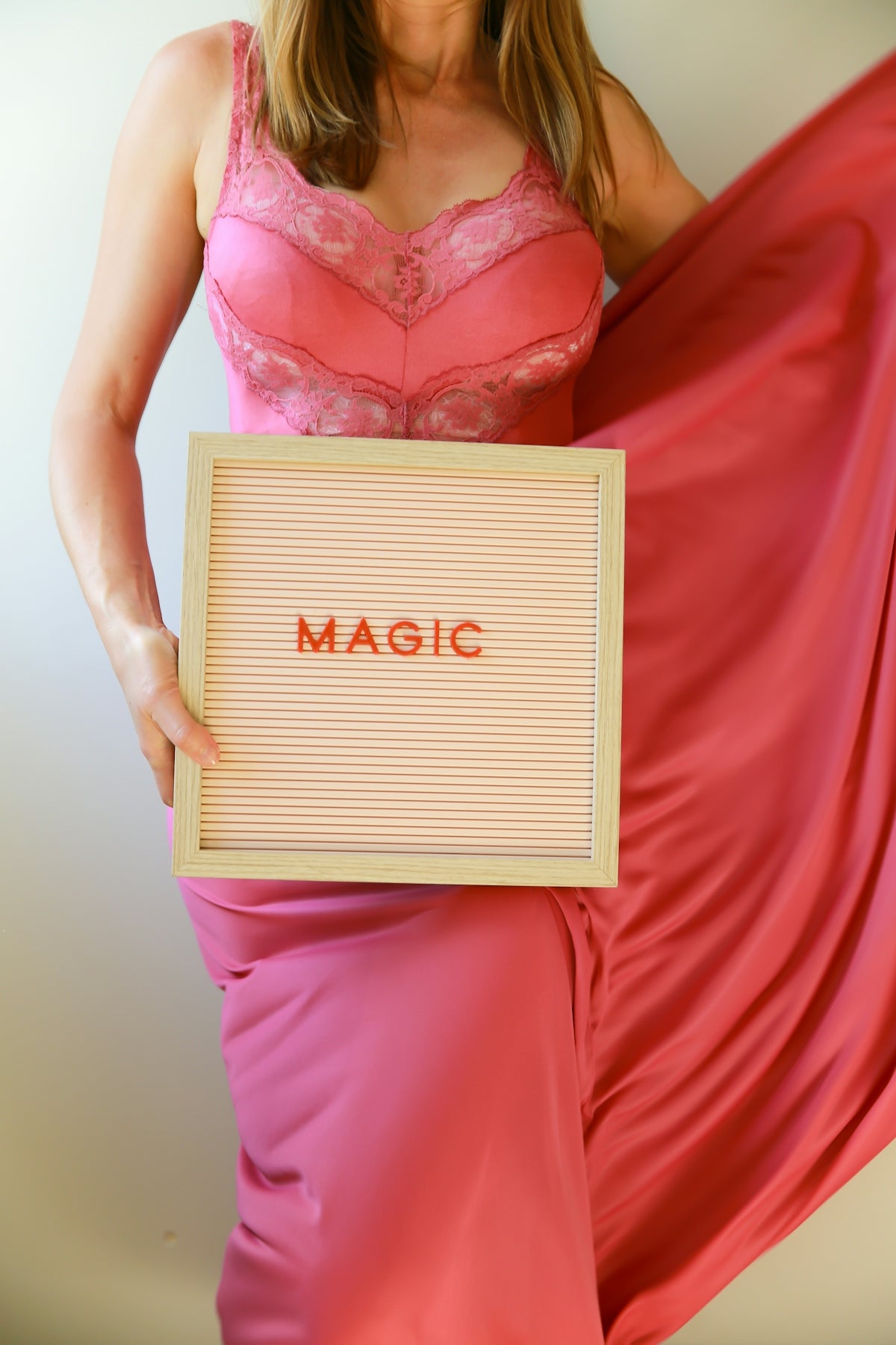 Woman in pink dress holds a sign reading magic.