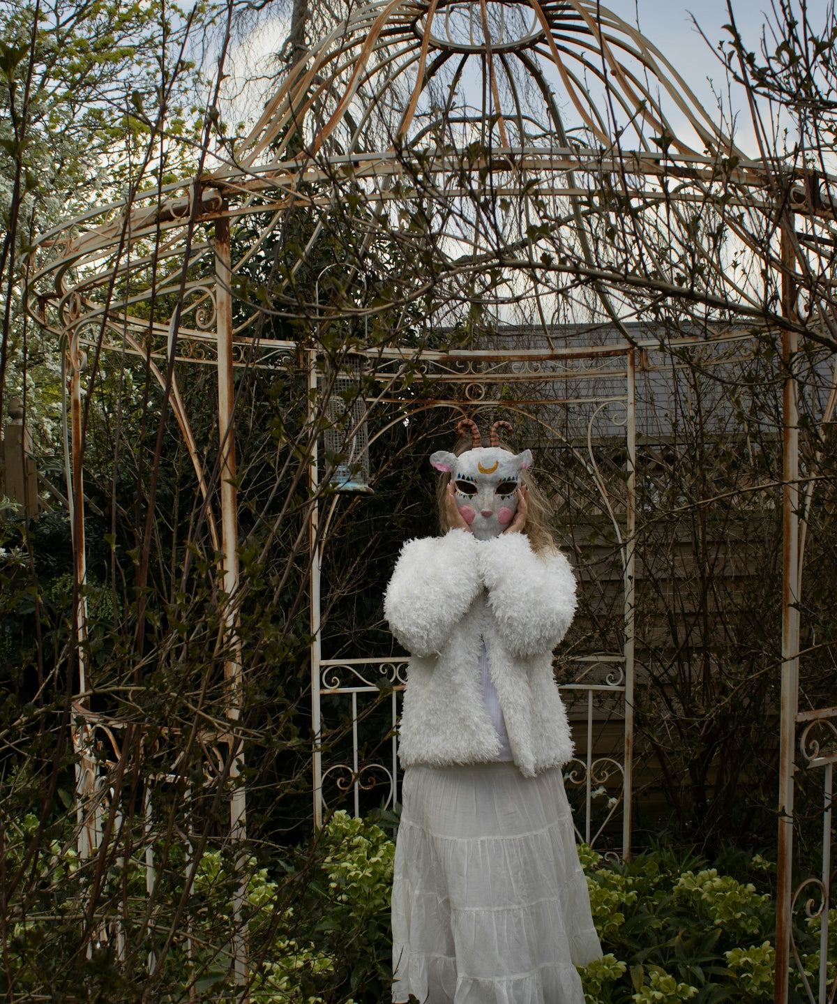 Person in animal mask and white coat in garden.