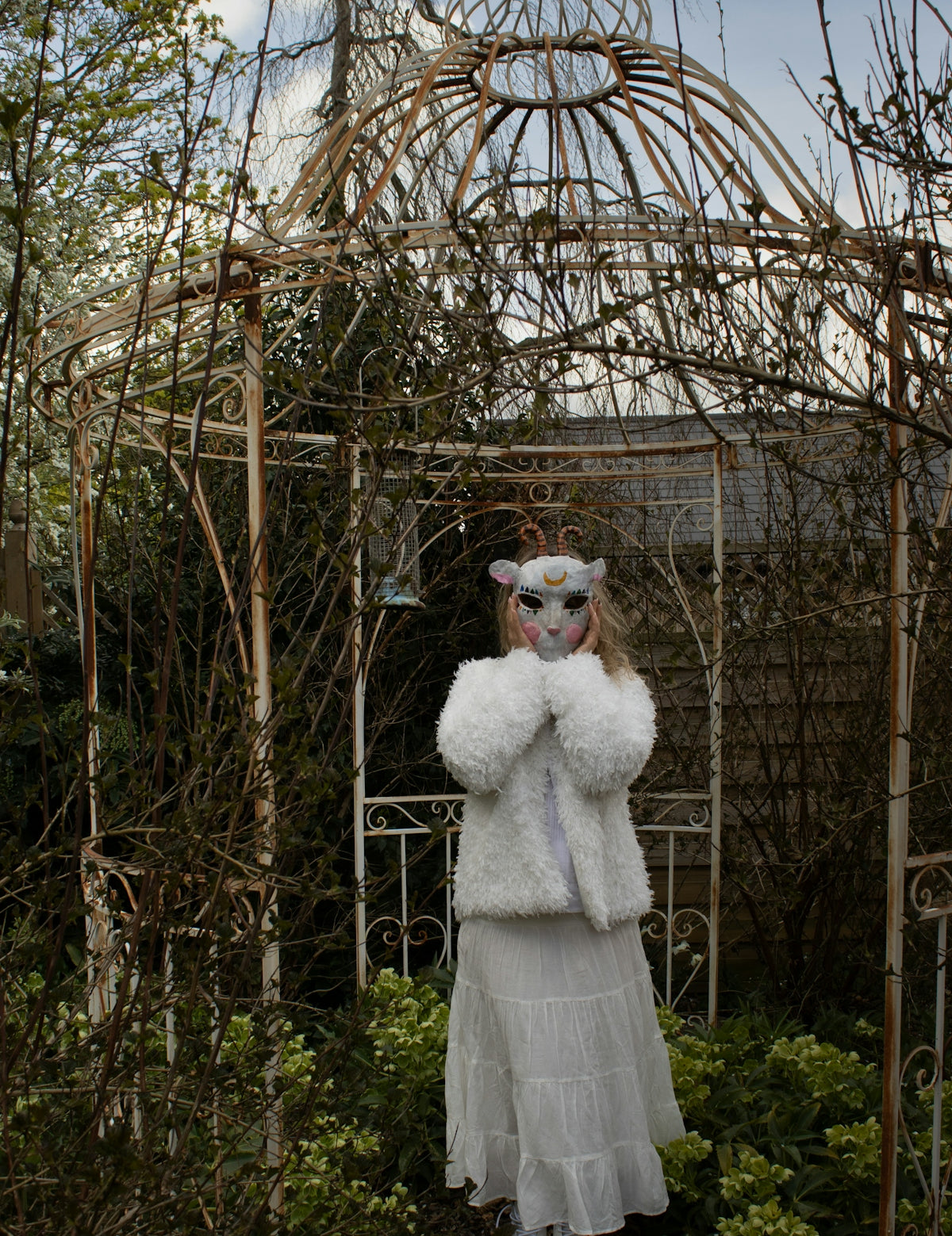 Person in animal mask and white coat in garden.