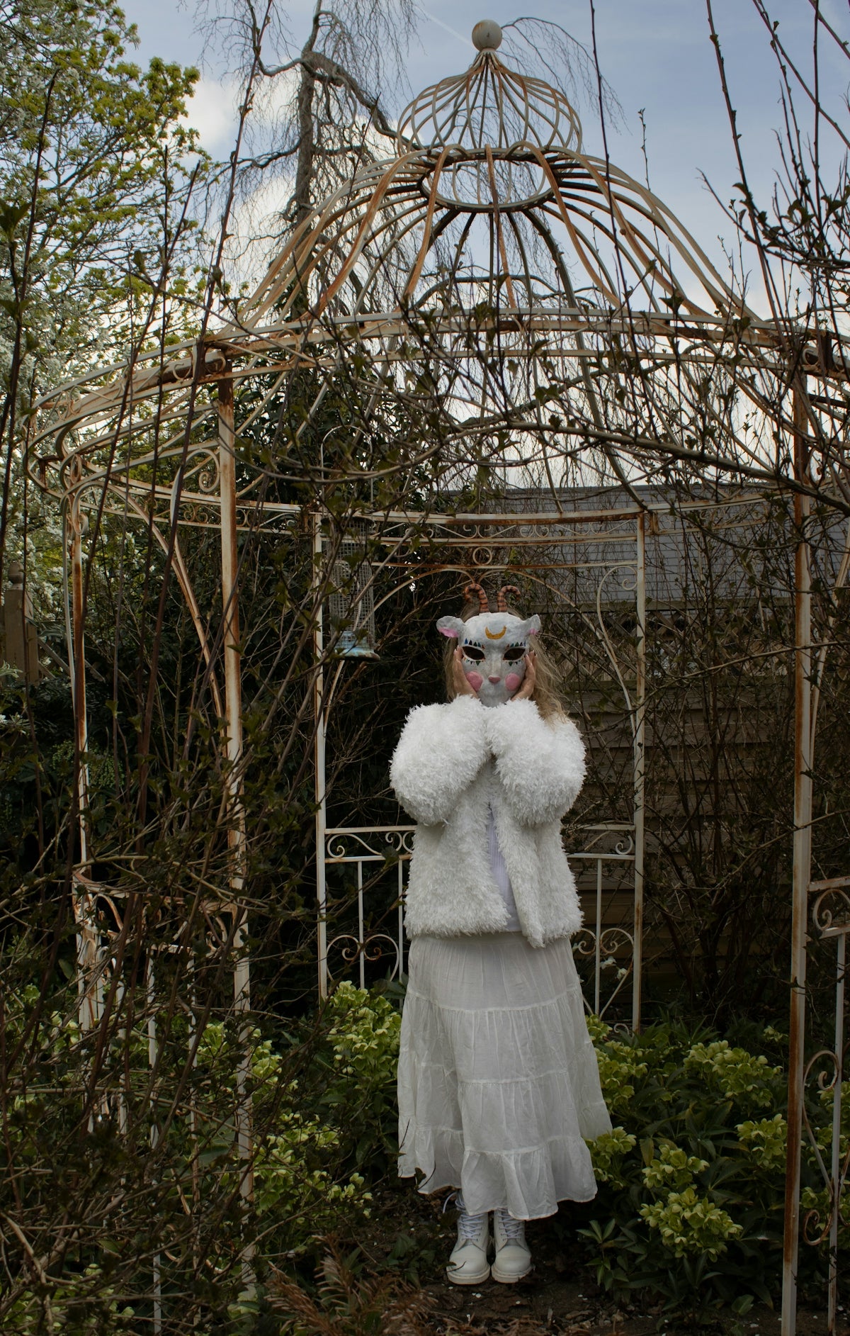 Person in animal mask and white coat in garden.
