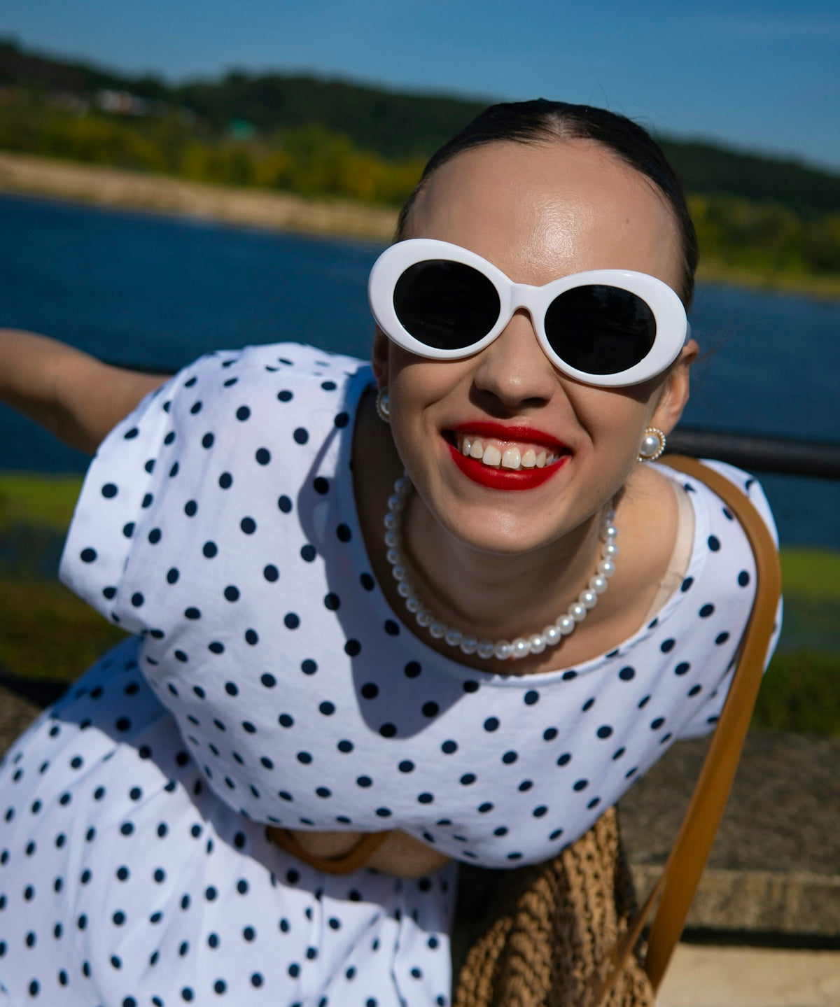Woman in polka dot dress with white sunglasses smiles.