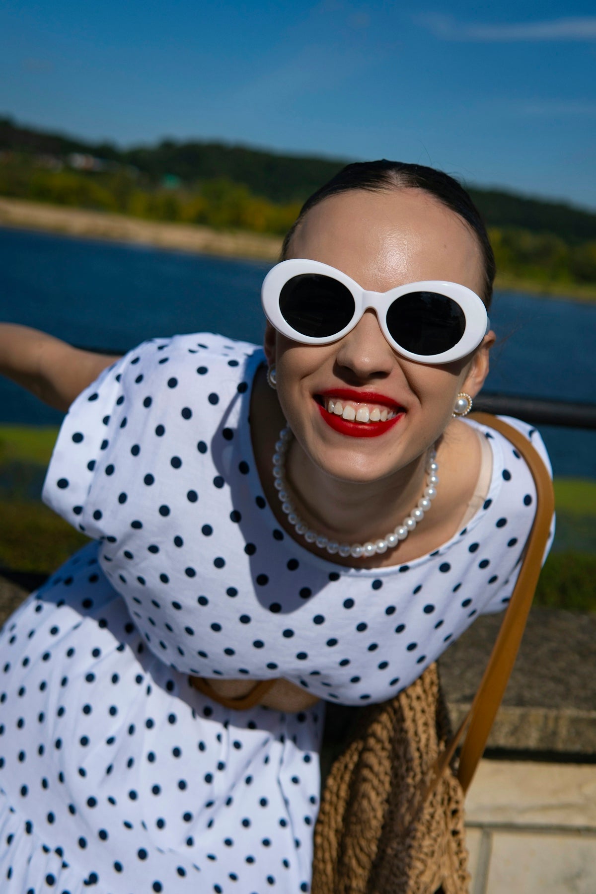 Woman in polka dot dress with white sunglasses smiles.
