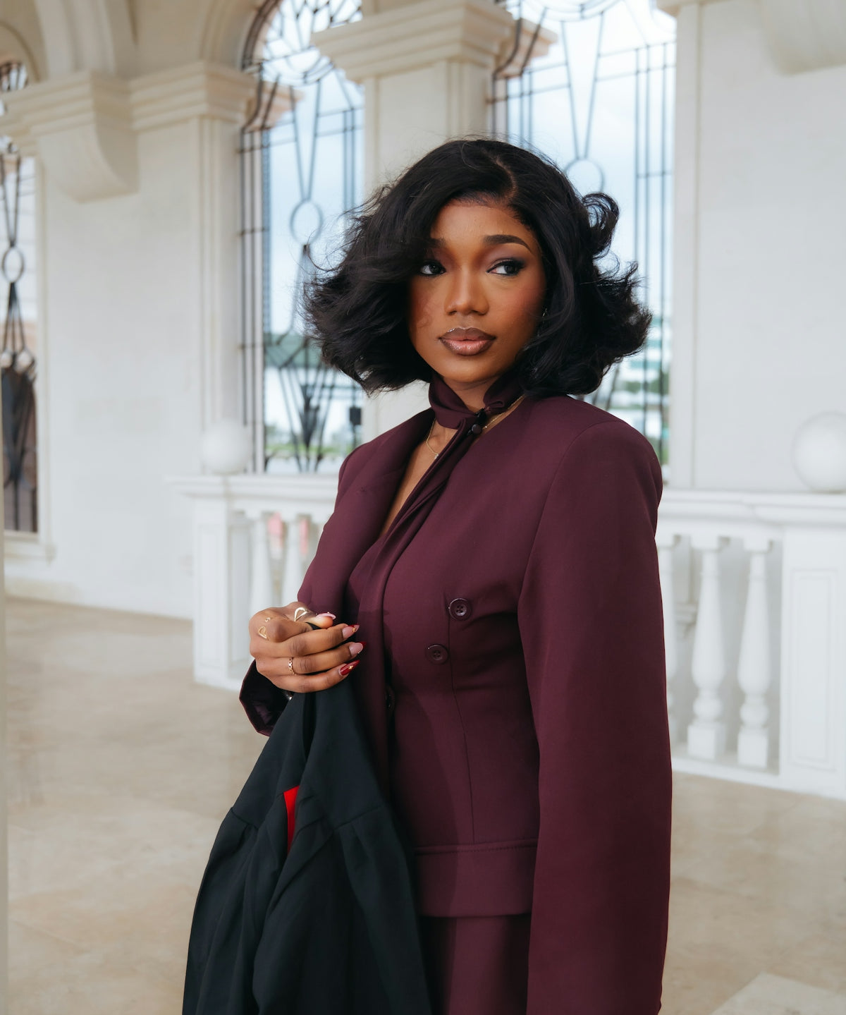 A woman in a maroon suit holding a black jacket.