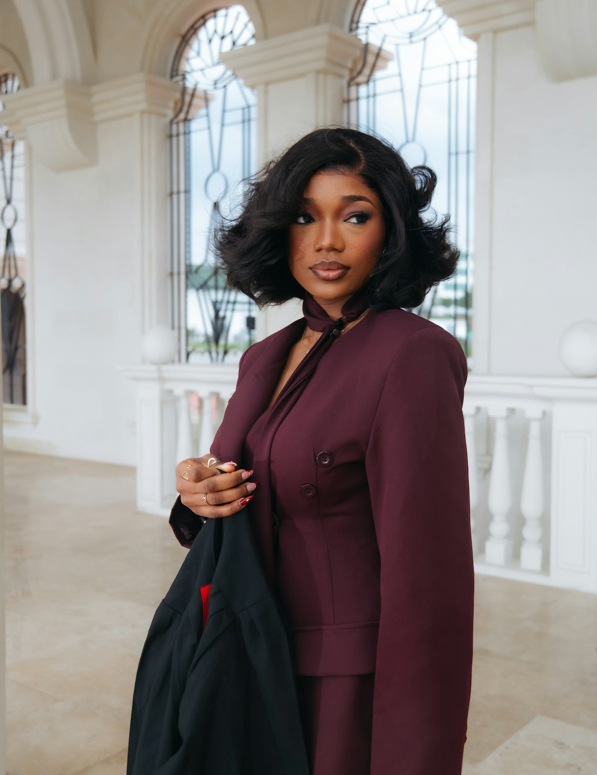 A woman in a maroon suit holding a black jacket.