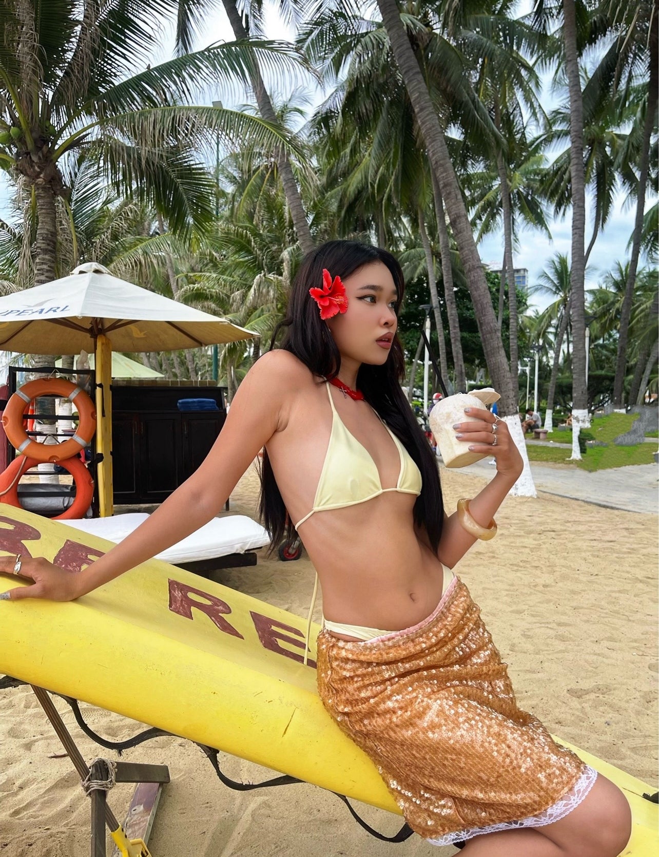 Woman on beach wearing Lily Sequin Midi Skirt in Light Brown, sequin womens skirt shines under palm trees.